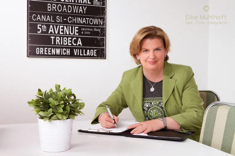 Unternehmerin im grünen Blazer notiert am Tisch, NYC-Straßenschild im Hintergrund