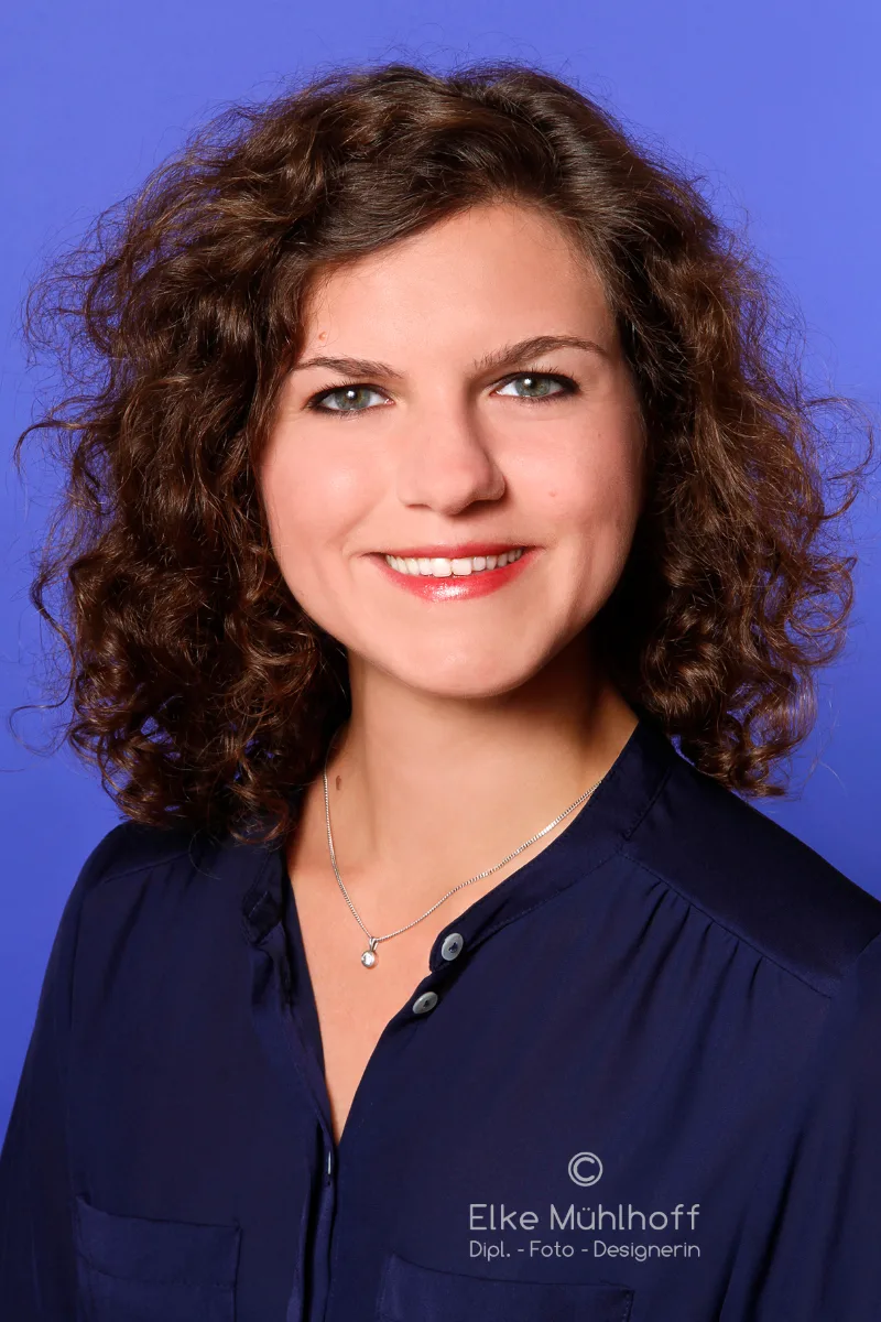 Headshot einer jungen Frau mit lockigen Haaren vor blauem Studiohintergrund