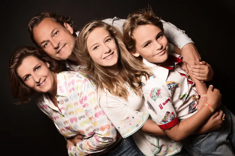 A family of four leaning close together in colourful patterned shirts against a black background