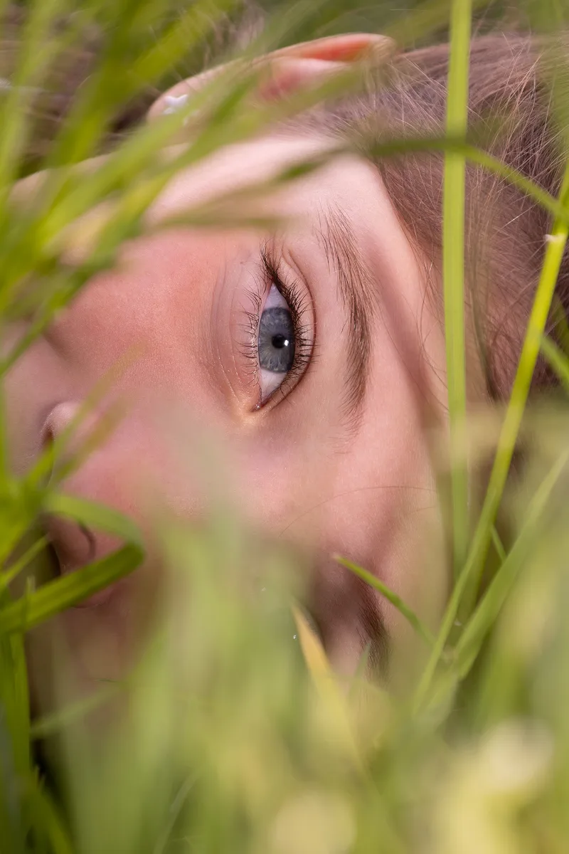 A close-up of a child's face lying in meadow grass, one blue eye in sharp focus
