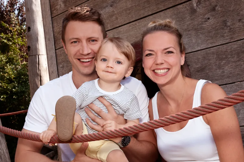 A young family with their toddler at a wooden playground in warm evening light