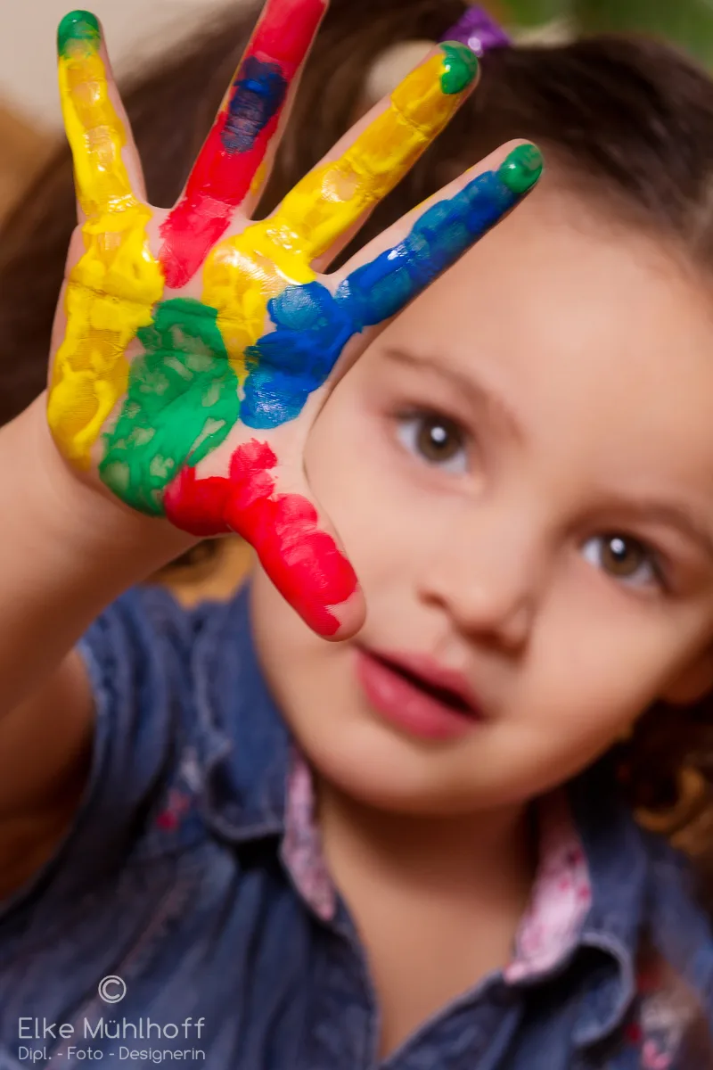 Kleines Kind hält ihre mit bunten Farben bemalte Hand in die Kamera