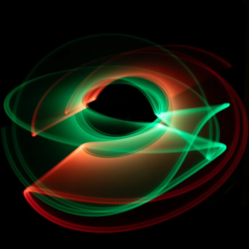 Light painting: green and red light trails looping in orbits on black