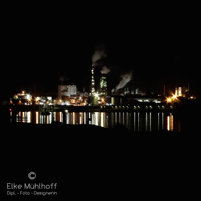 Illuminated industrial complex on the waterfront during the blue hour, lights reflecting in the river