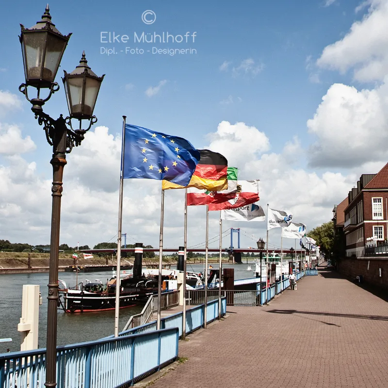 Sunny Rhine promenade with a row of fluttering flags, an ornate old street lamp and an excursion boat