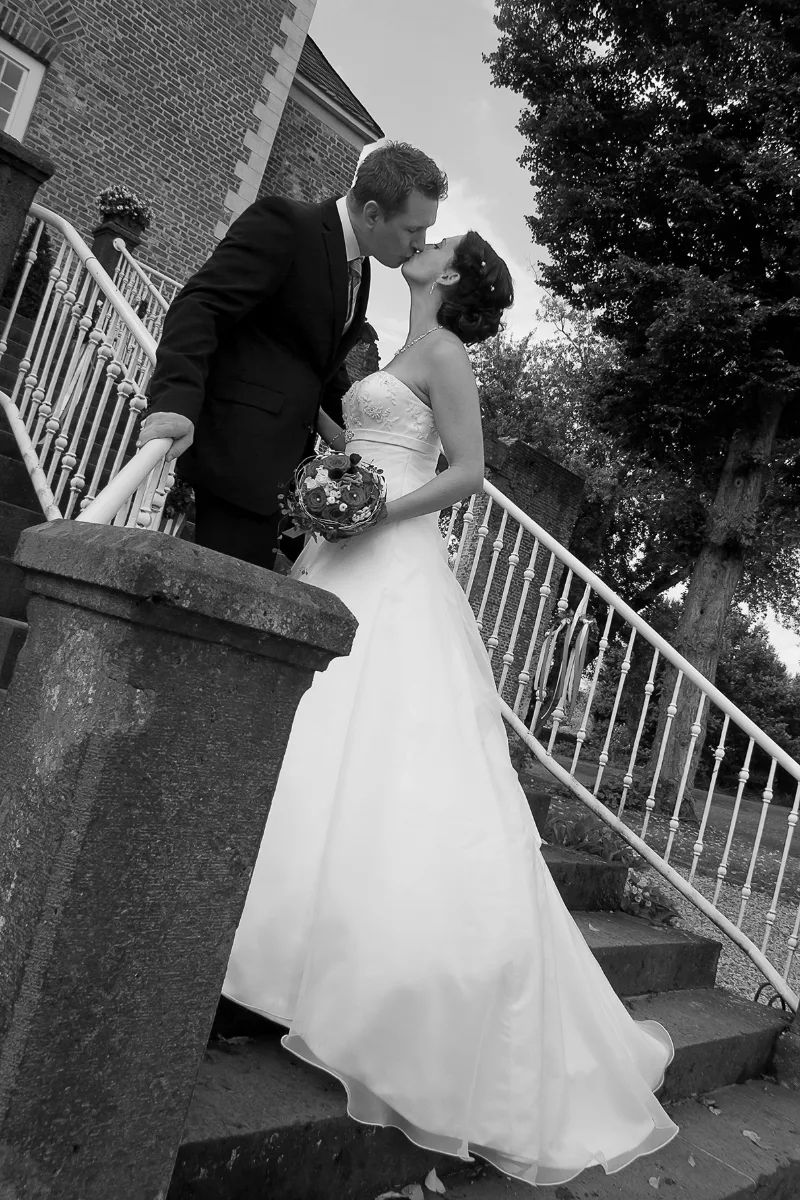Bride and groom kissing in front of a grand classicist castle in a sunny castle park