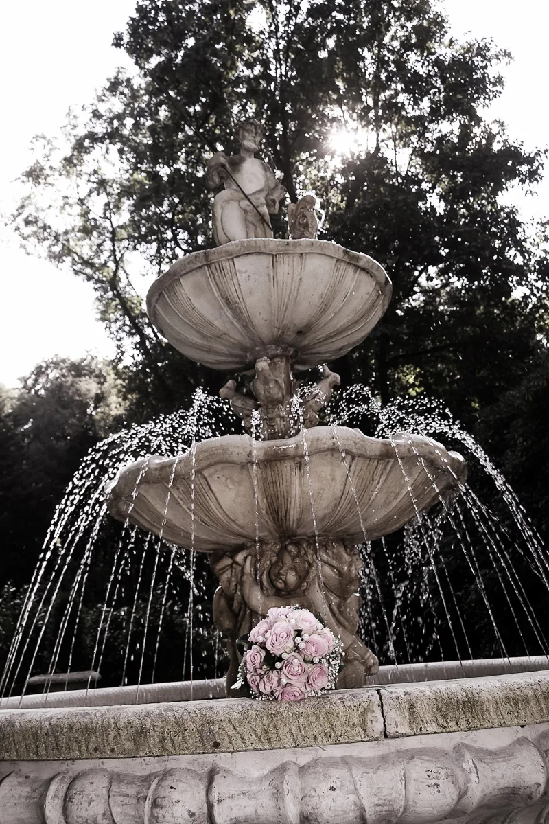 A pink bridal bouquet resting on the rim of an old fountain — a close-up detail